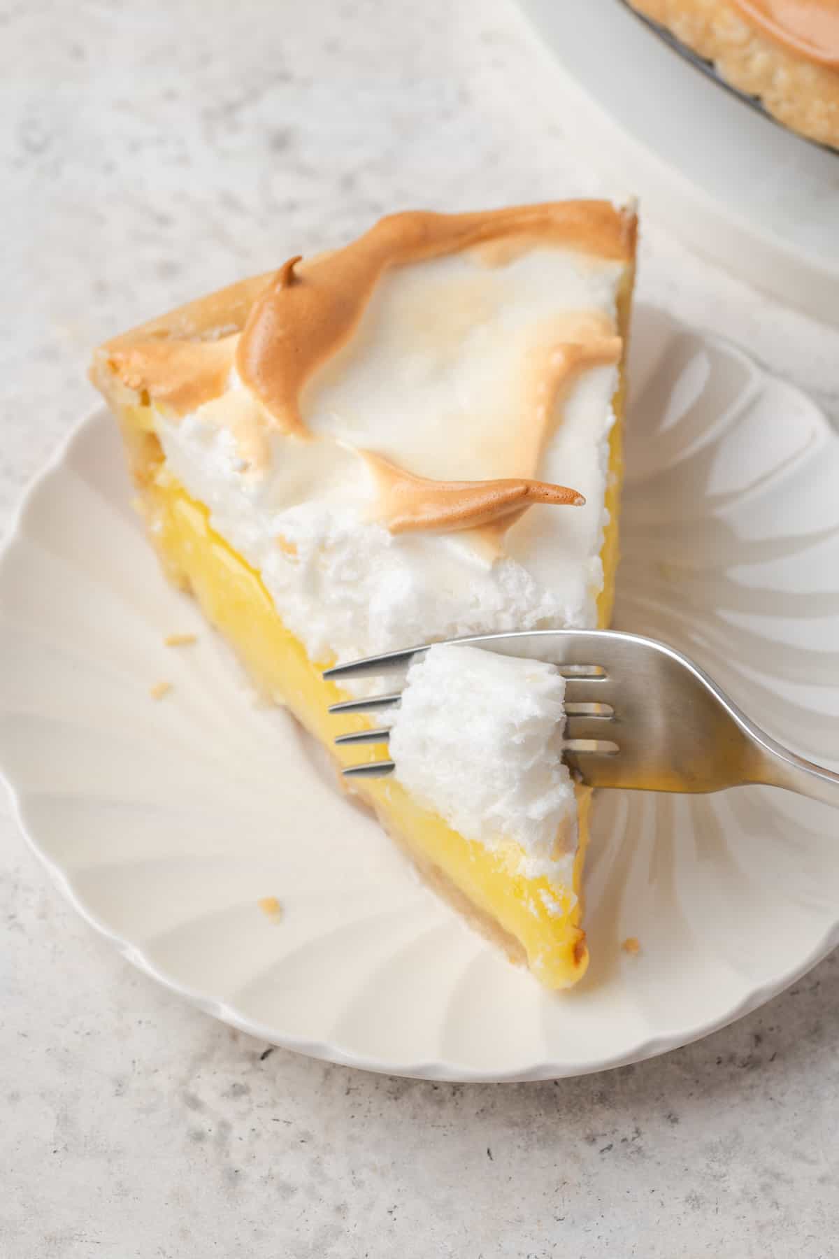 A fork cuts into a slice of gluten free lemon meringue pie on a white plate.