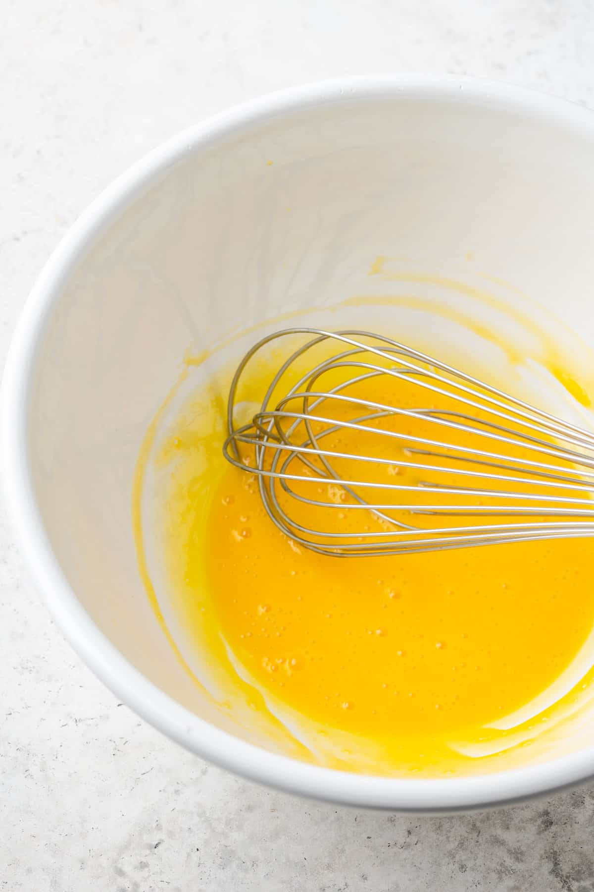 A whisk mixes egg yolks in white bowl.