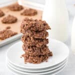 A stack of no bake chocolate oatmeal cookies is shown with milk in the background.
