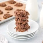 A stack of no bake chocolate oatmeal cookies is shown with milk in the background.