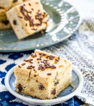 A close up of a chocolate chip cookie bar with a plate of bars in the background.