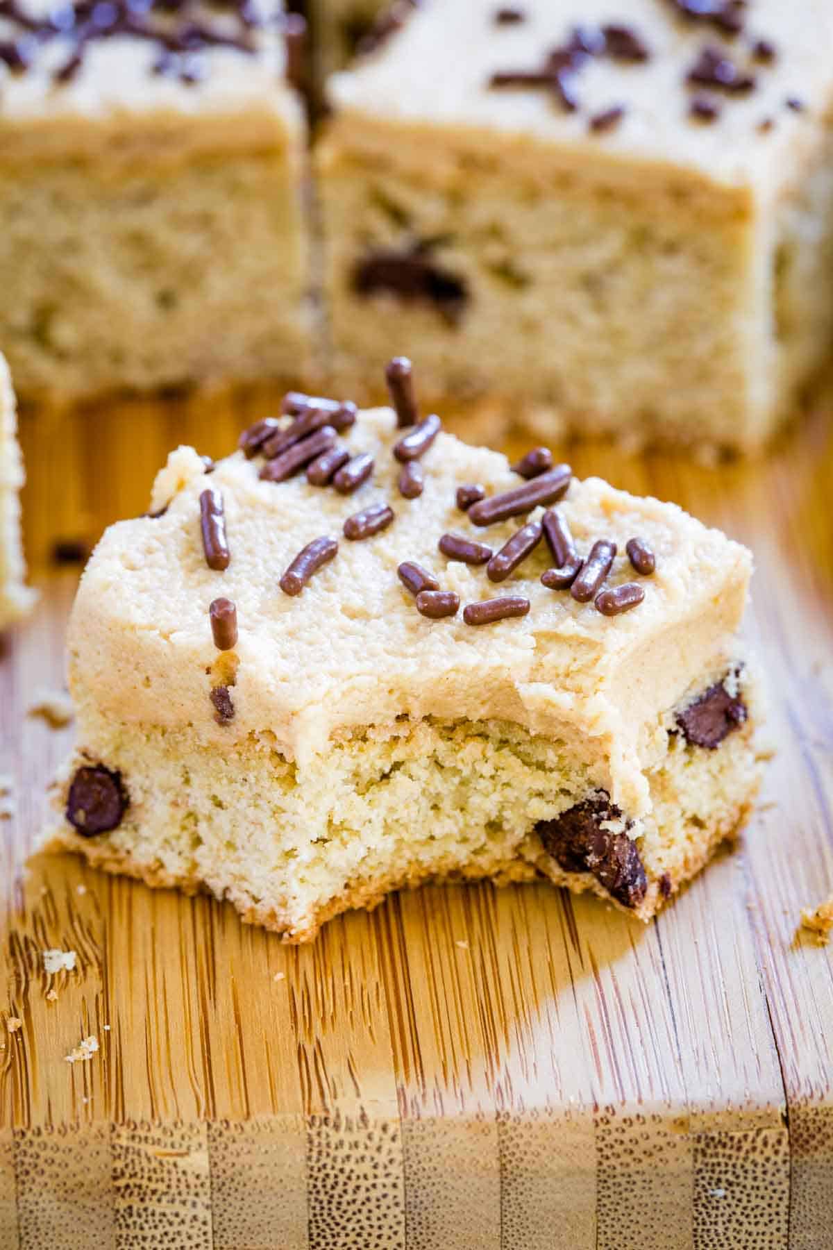 A chocolate chip cookie bar on a wooden board with a bite taken out.