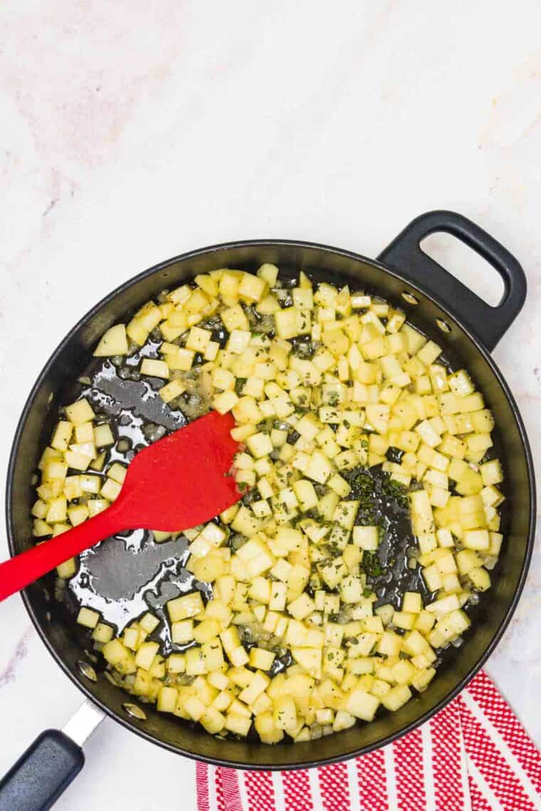A skillet full of chopped apples with a red spatula.