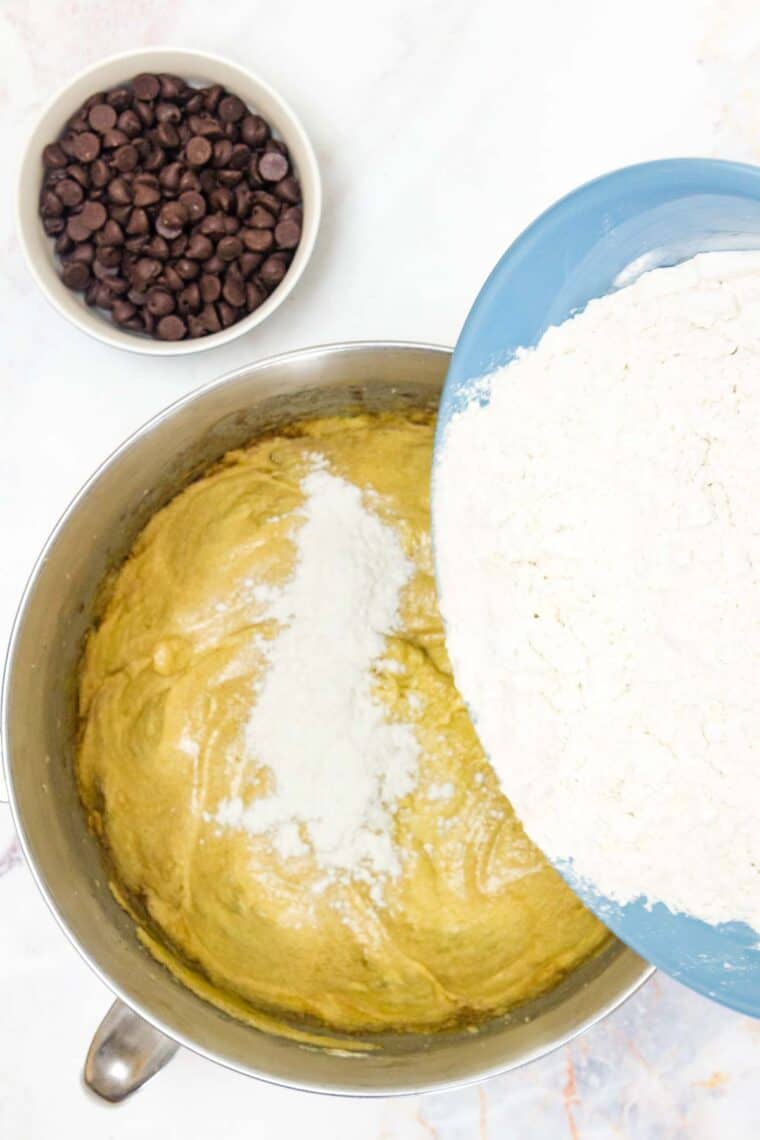 A bowl pours flour mix into a bowl of wet mix for chocolate chip cookie bars.