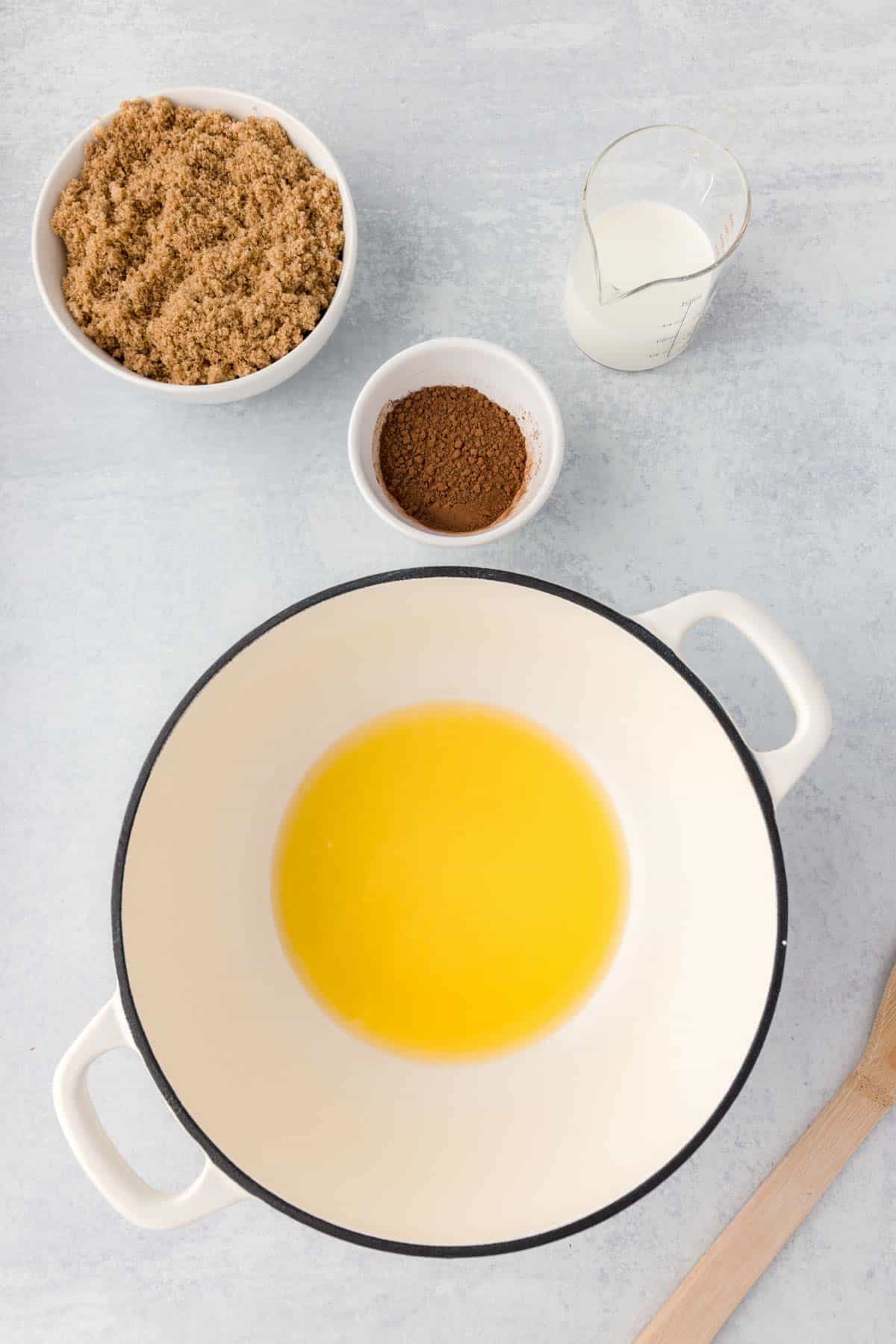 Melted butter is shown in a pot with brown sugar, milk, and cocoa powder next to it.