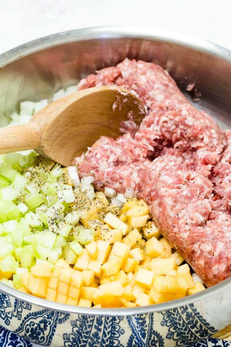 A spoon cooks pork sausage in a skillet with celery and apples.