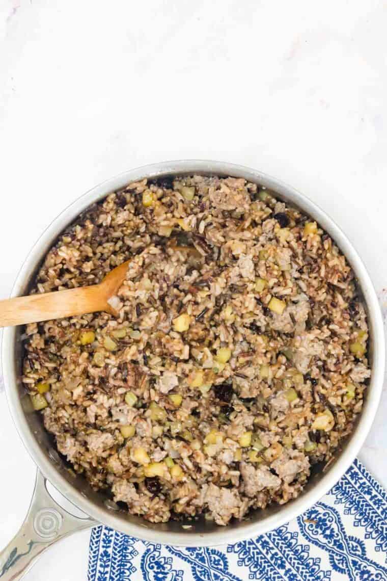 A wooden spoon stirs a skillet of wild rice stuffing.