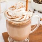 A glass of Mexican hot chocolate topped with whipped cream and a cinnamon stick.