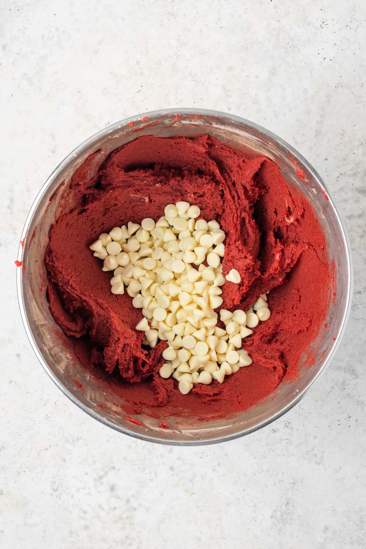White chocolate chips are added to a bowl of gluten free red velvet cookie dough.