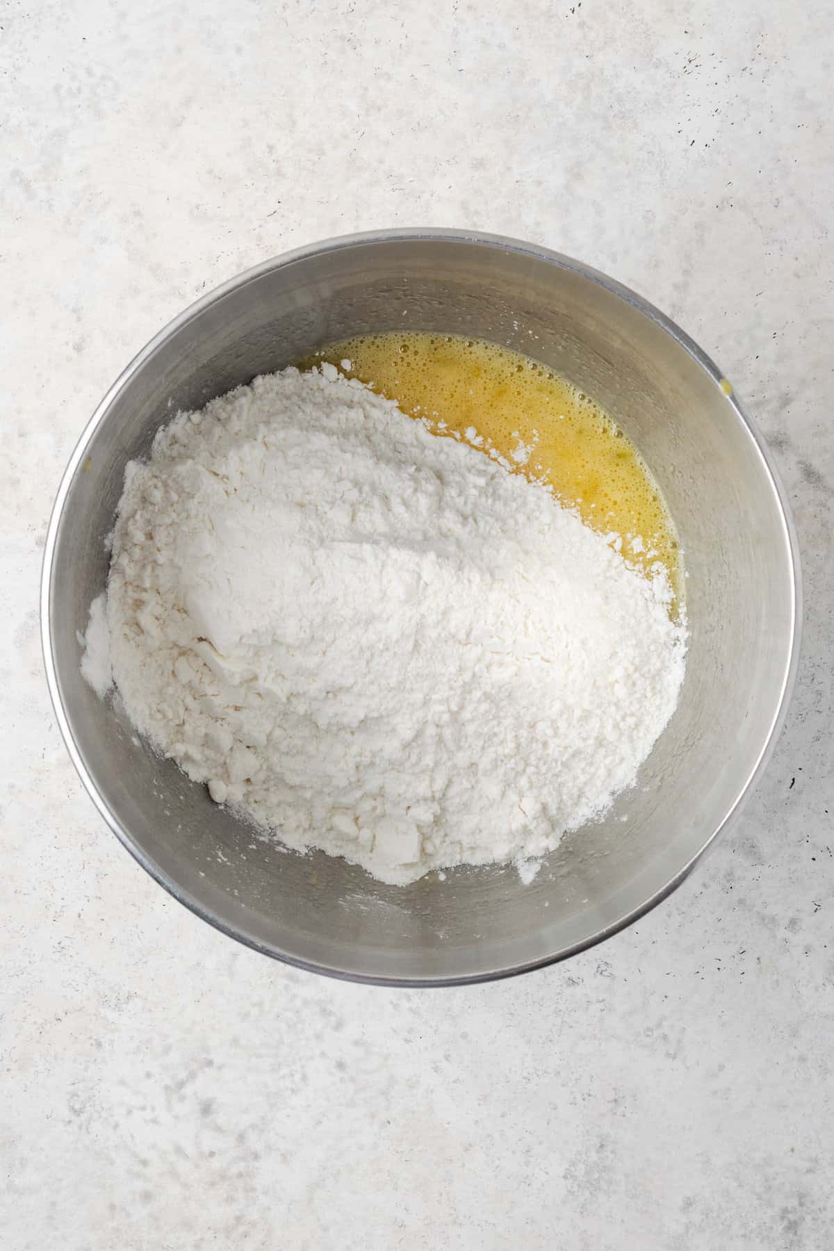 Gluten free bread mix is added to the wet mix in a metal bowl.
