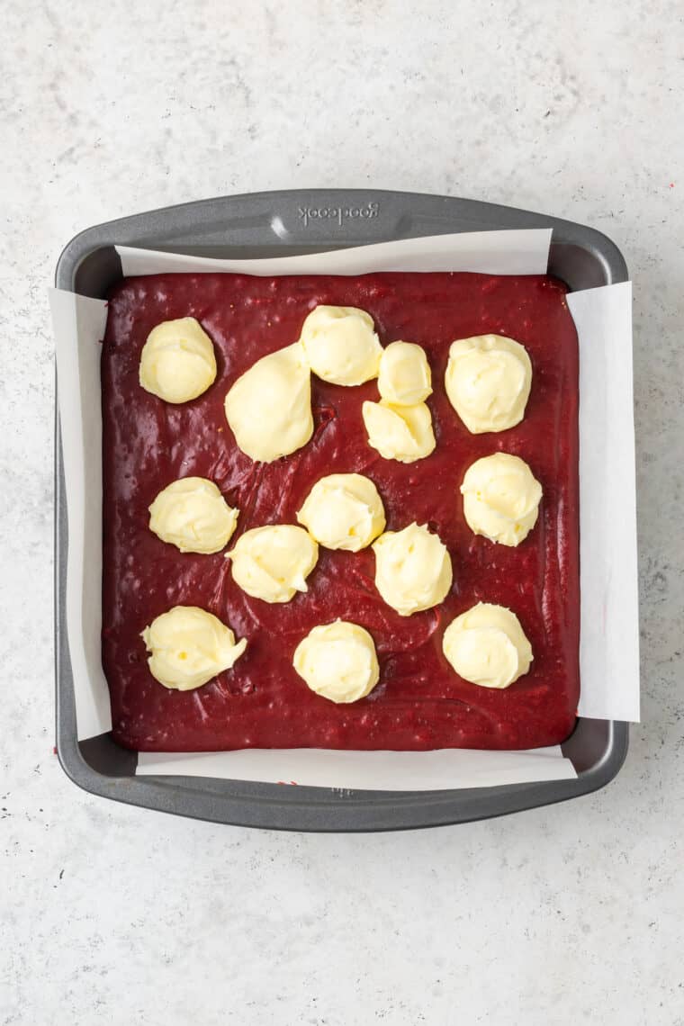 A top down shot of a pan of red velvet brownie batter with cream cheese dotted on top.