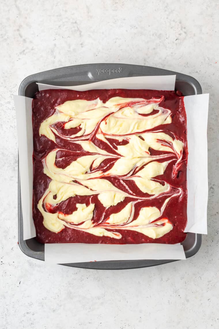 Decorative cream cheese swirls in red velvet brownie batter.