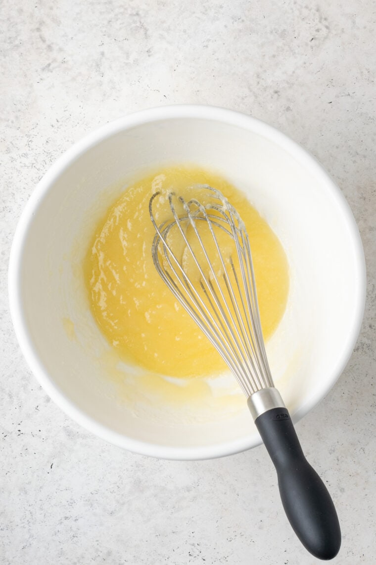 A whisk mixes butter and suggar in a white bowl.
