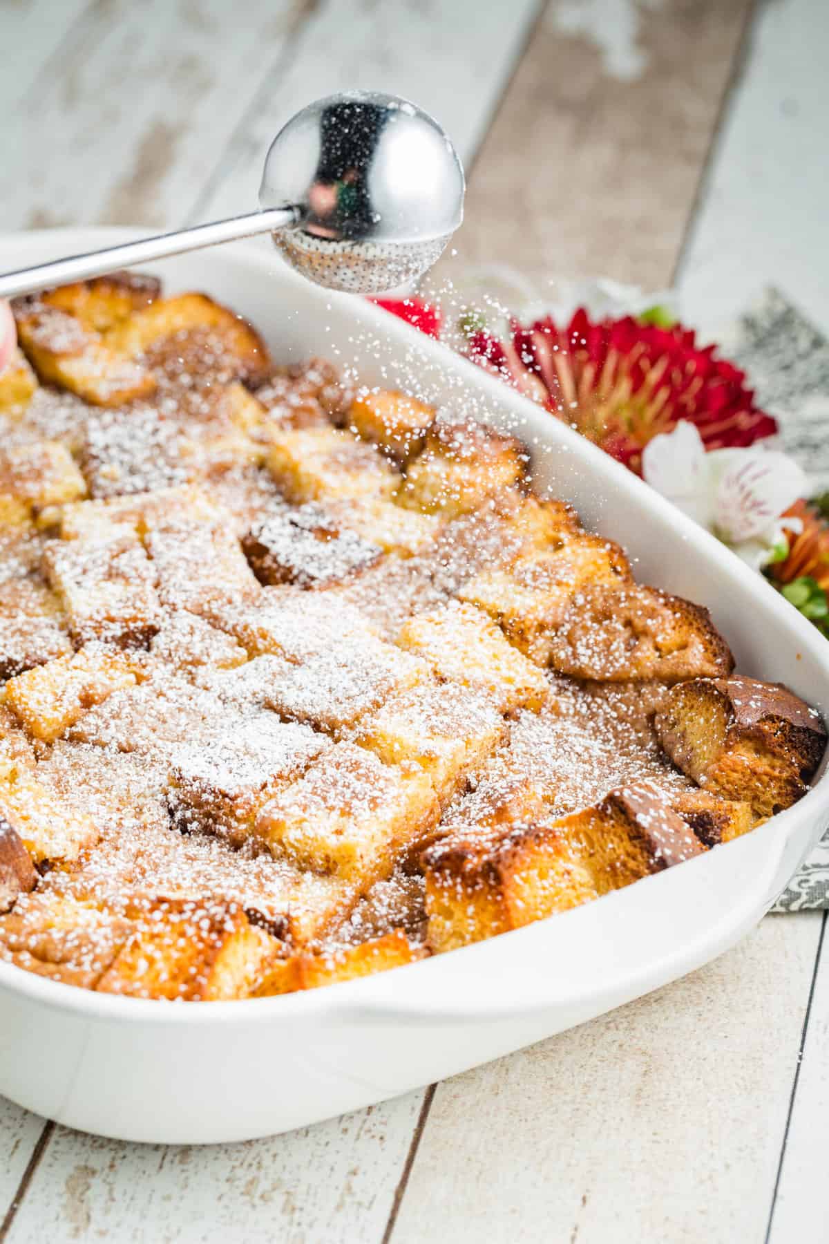 Powdered sugar being sprinkled over french toast casserole.
