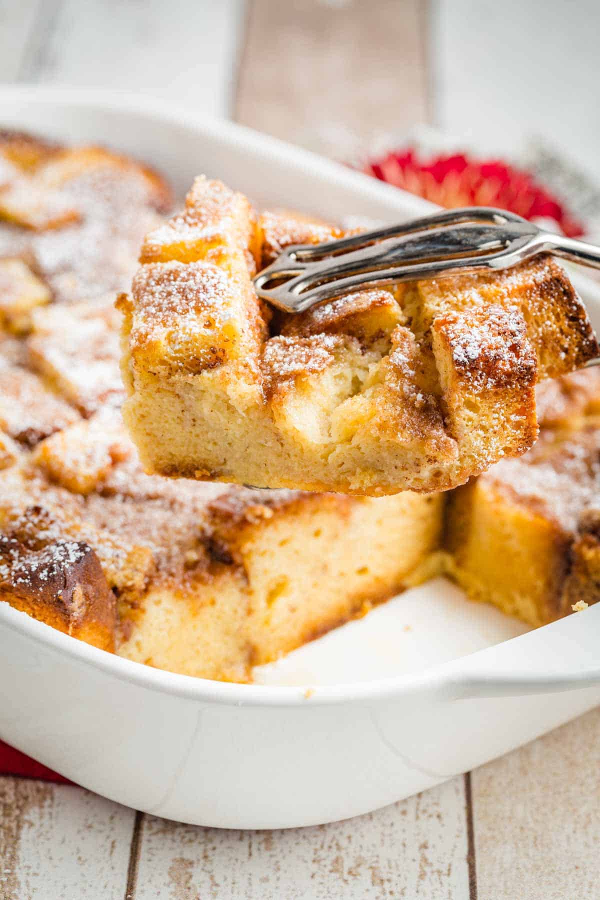 A metal serving utensil lifts out a piece of French toast casserole from a white baking dish filled with the full casserole.