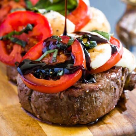 Balsamic vinegar reduction is drizzled over grilled steaks topped with alternating slices of fresh mozzarella and tomatoes.