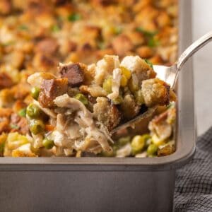 A serving spoon scooping chicken stuffing casserole out of a baking dish.