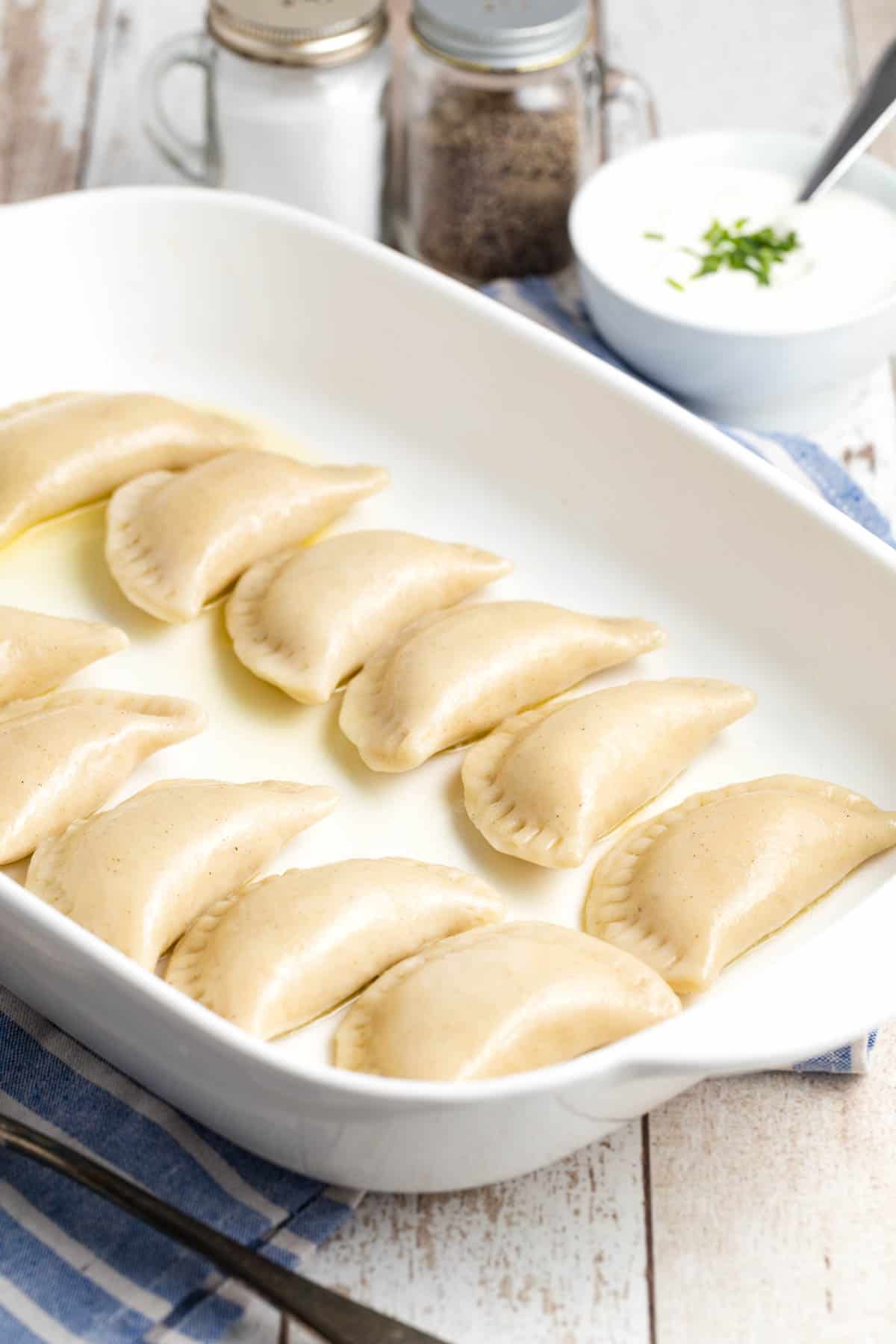 A white baking dish filled with uncooked pierogi.
