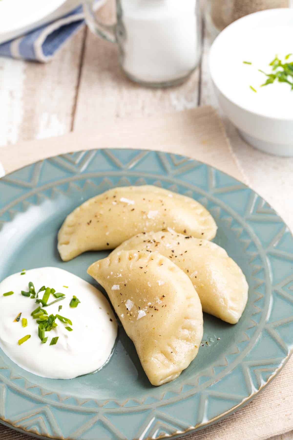 A blue plate of pierogi and sour cream topped with parsley.