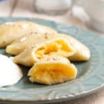 A plate of pierogi with one cut open to show the potato filling and sour cream.