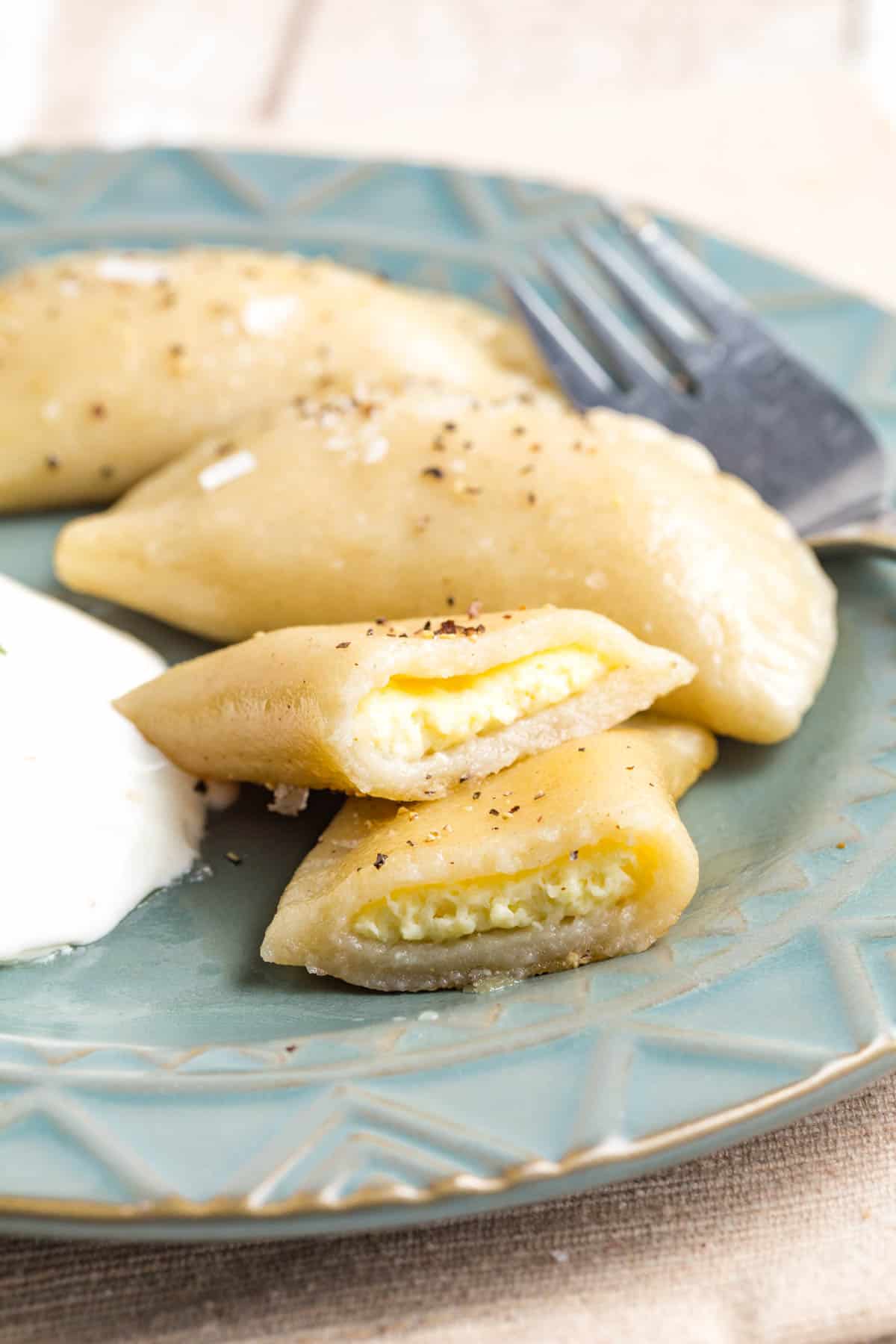 A plate of pierogi with one cut open to show the pot cheese filling and sour cream.