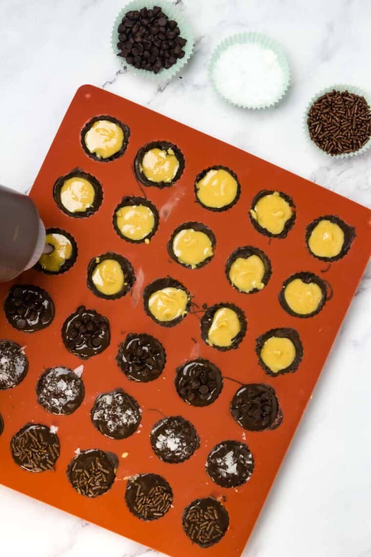 Peanut butter is added to chocolate cups in a silicone tray.