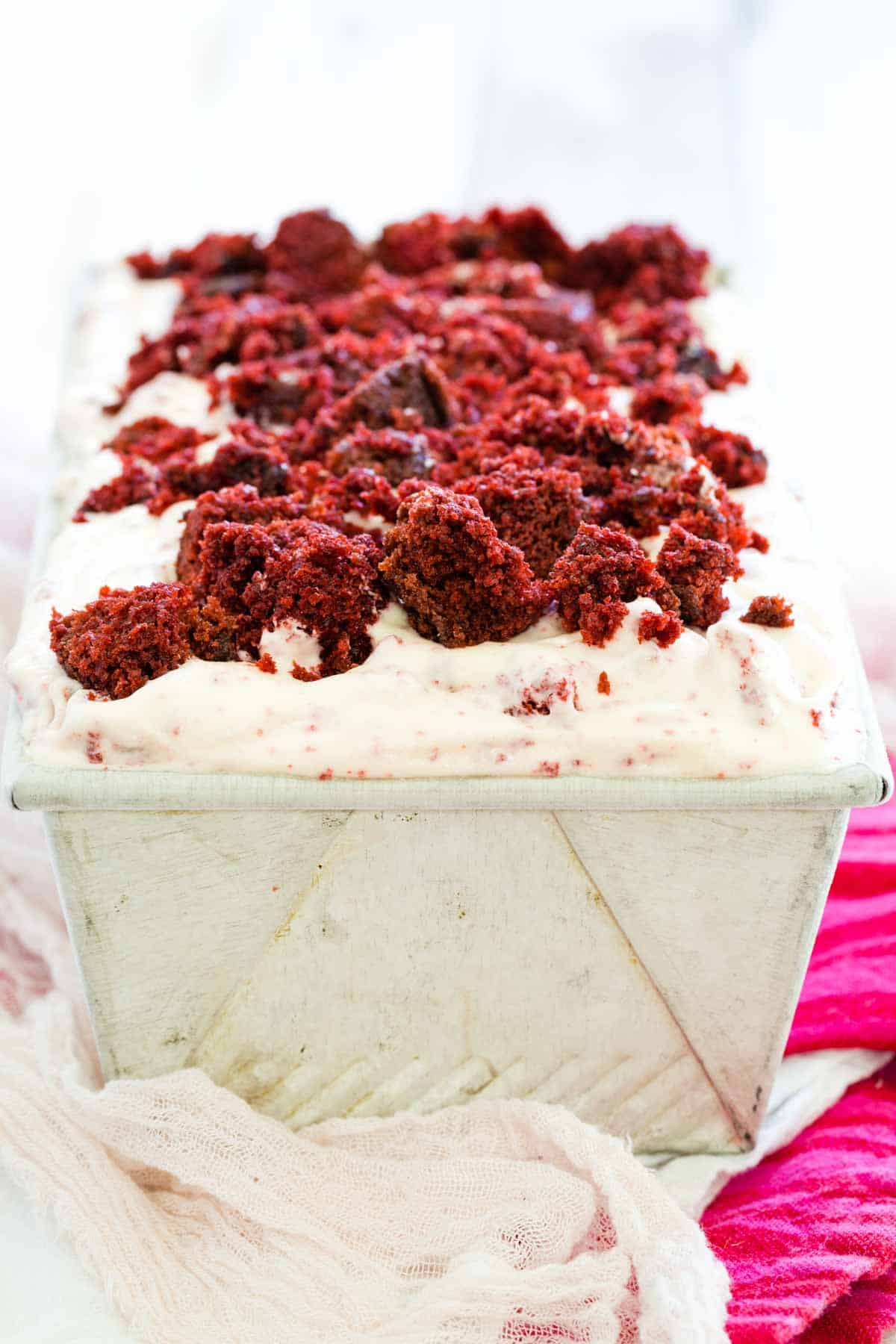 A loaf pan of ice cream topped with chunks of red velvet cake.