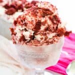 Red and white scoops of velvet ice cream are shown in a glass ice cream dish on a red napkin with a spoon next to it.