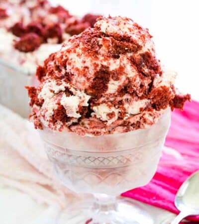 Red and white scoops of velvet ice cream are shown in a glass ice cream dish on a red napkin with a spoon next to it.
