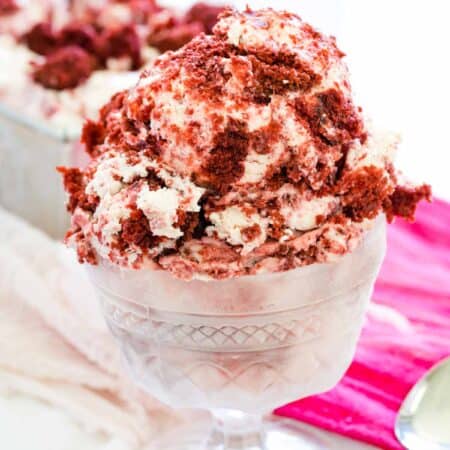 Red and white scoops of velvet ice cream are shown in a glass ice cream dish on a red napkin with a spoon next to it.