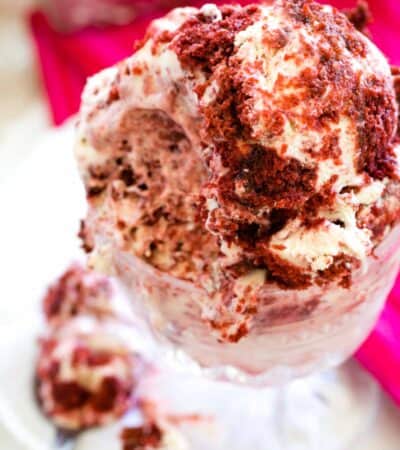 A close up shot of a glass bowl of red velvet ice cream that shows the red velvet cake crumbles in the white ice cream.