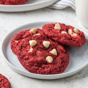 Three red velvet cookies with white chocolate chips on a small white plate.