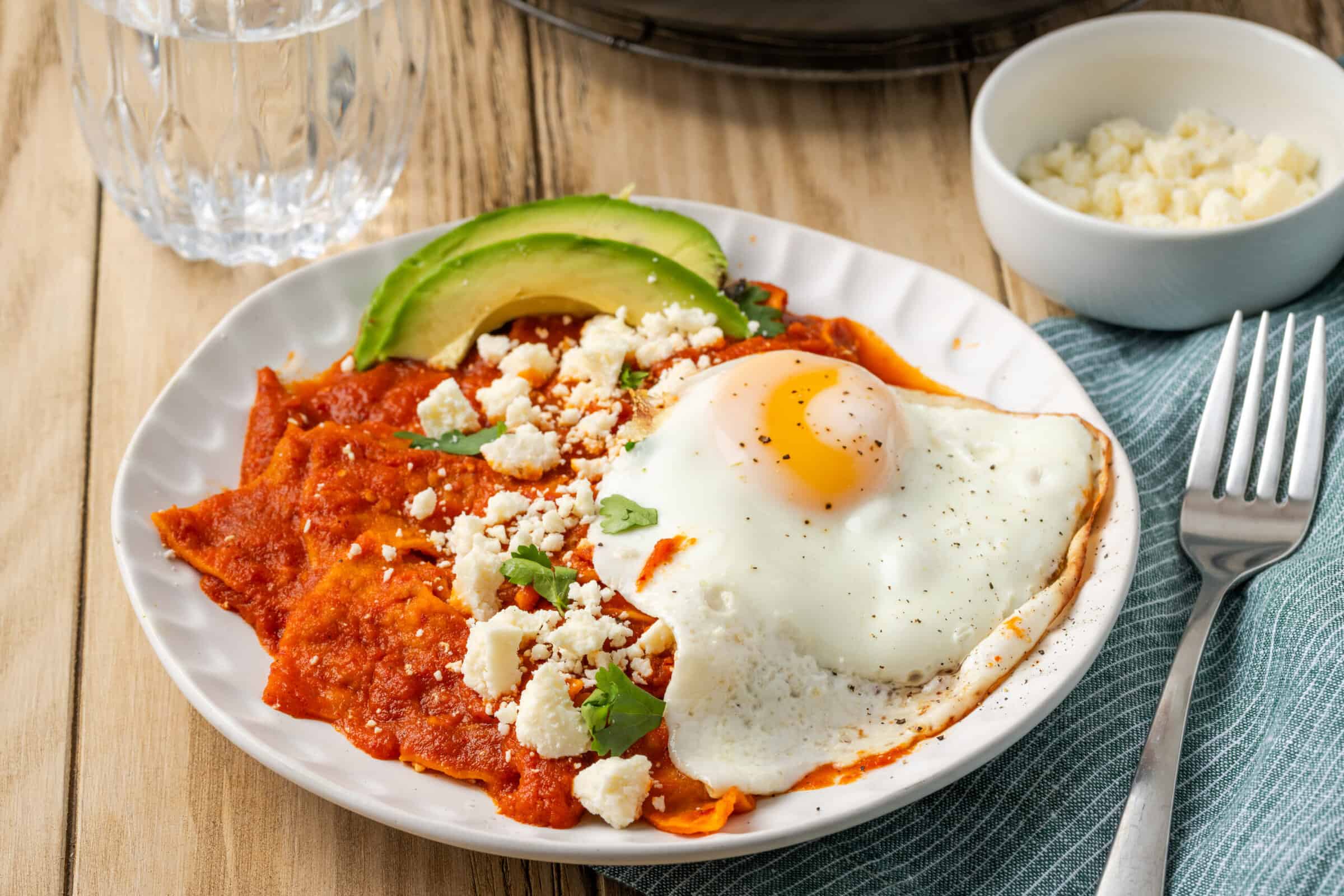 Chilaquiles rojos are shown on a plate with avocado and fried eggs.
