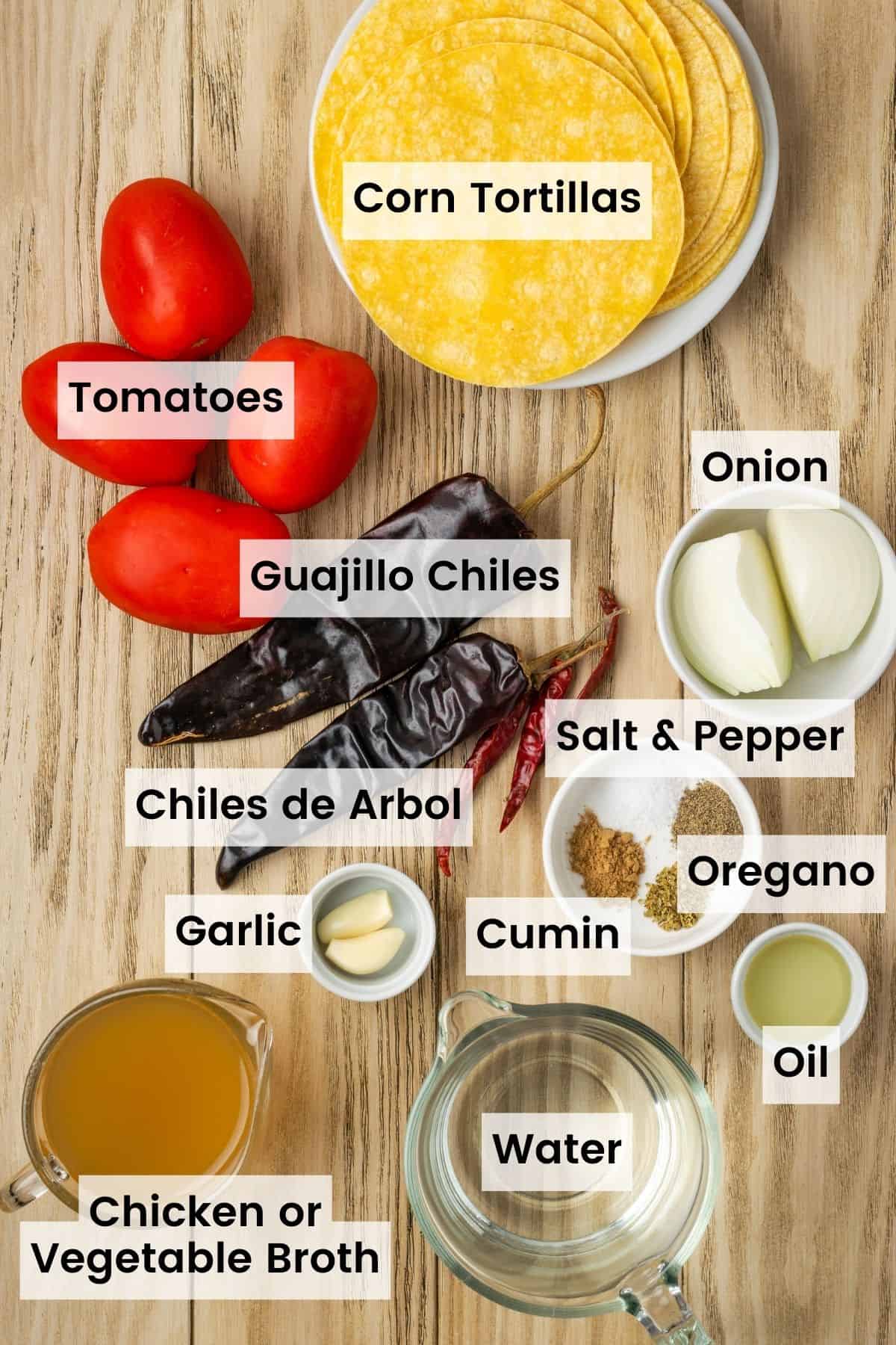 Ingredients for chilaquiles rojos with text labels are shown on a cutting board: roma tomatoes, onion, chiles, corn tortillas, cumin and oregano, salt and pepper, olive oil, and garlic.