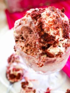 A close up shot of a glass bowl of red velvet ice cream that shows the red velvet cake crumbles in the white ice cream.
