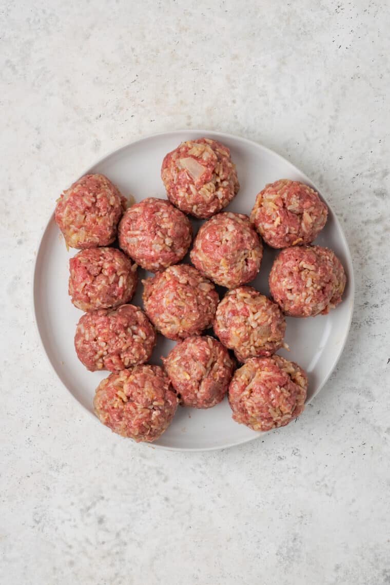 Formed but uncooked meatballs are shown on a white plate.