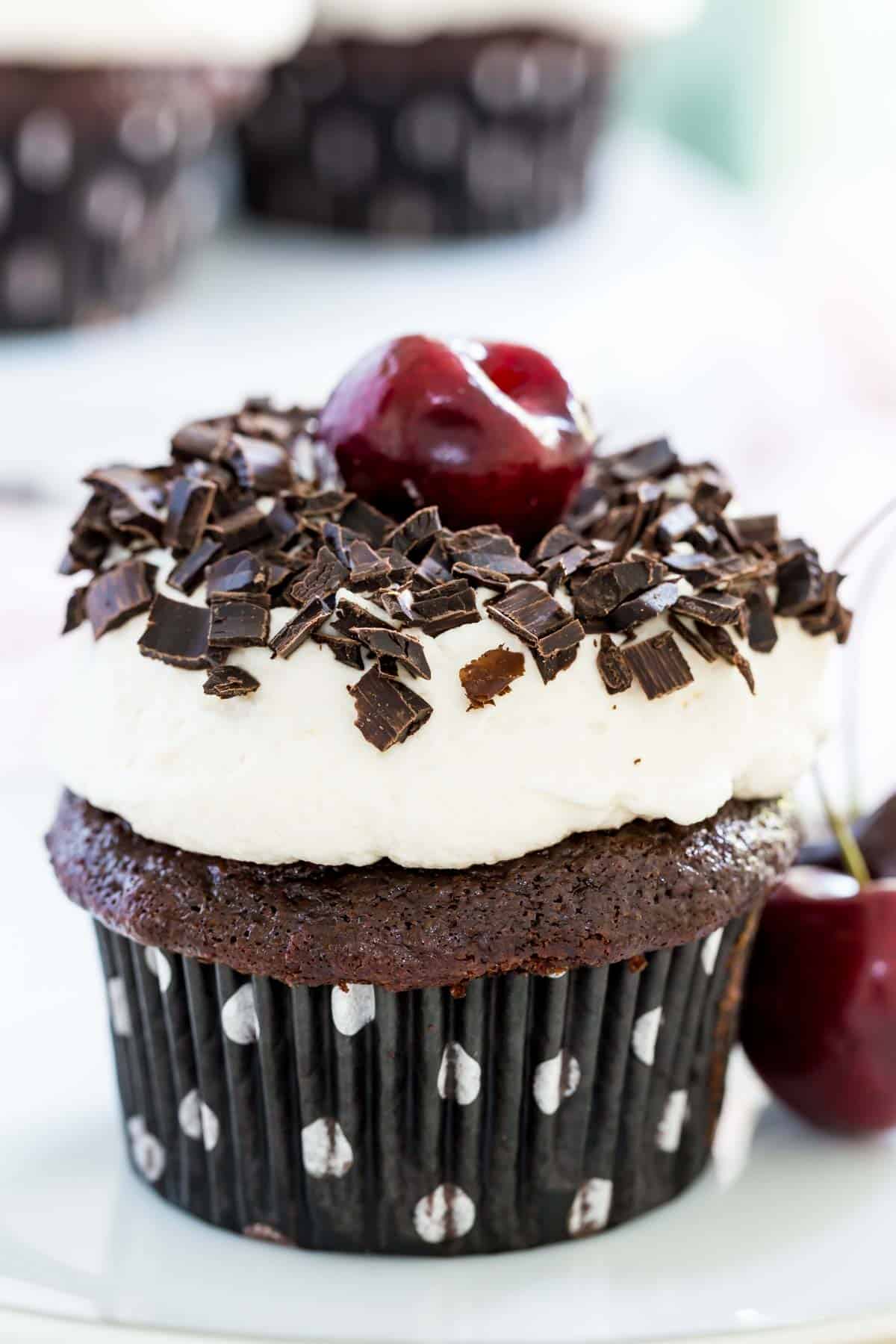 A black forest cupcake with a cherry next to it is on a white plate.