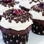 A fresh cherry sits on top of a black forest cupcake that's also garnished wtih chocolate.