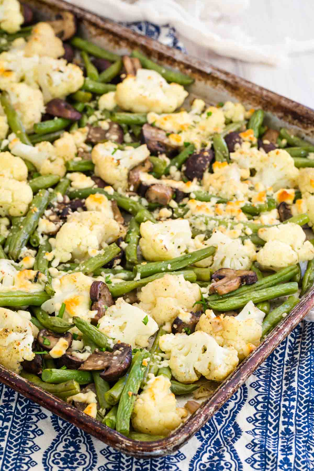 Blue cheese roasted vegetables including green beans and mushrooms are shown after the oven on a metal baking sheets.