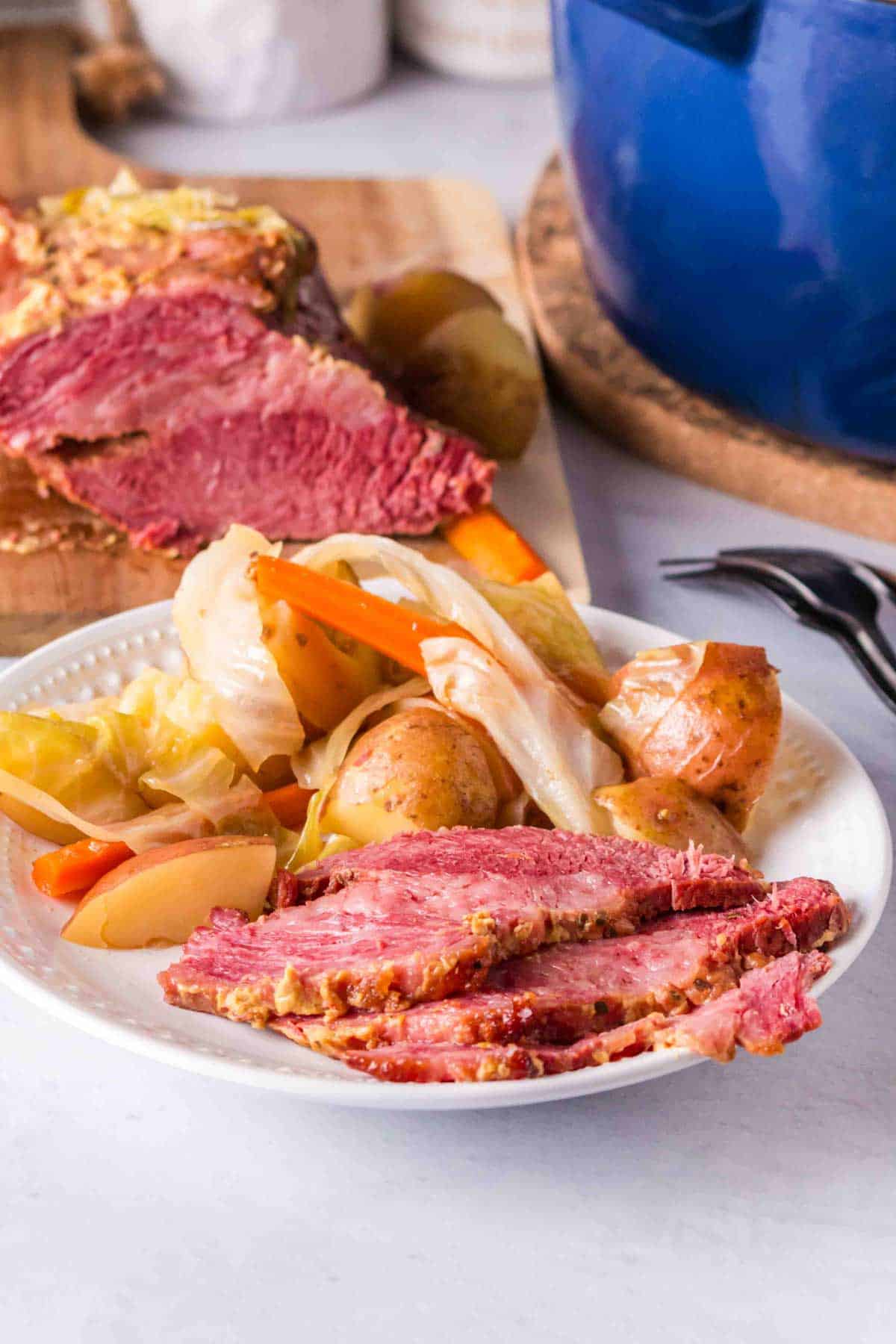 A plate of corned beef and cabbage on a counter with beef in the background.