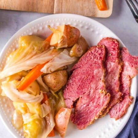 A white plate of corned beef with cabbage and potatoes on the side, and more beef in the background.