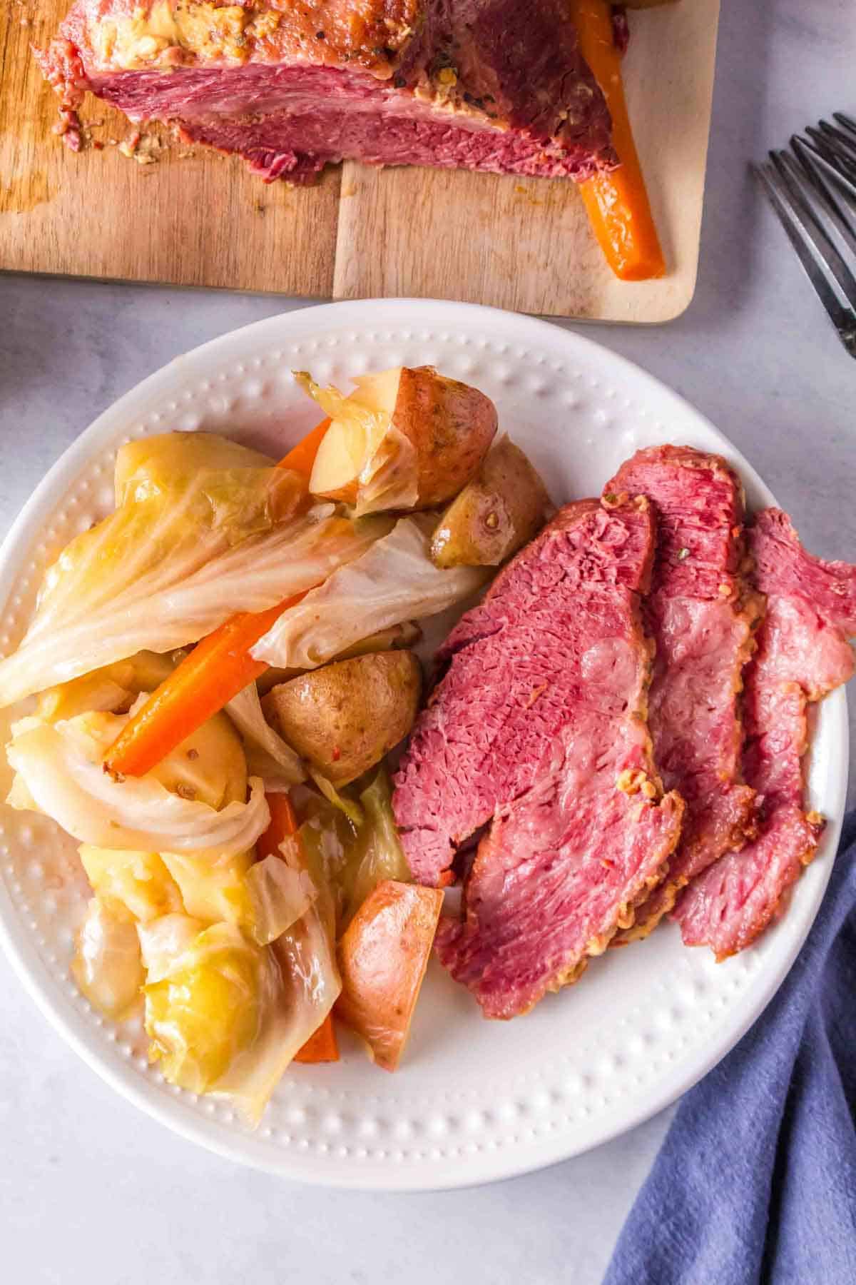 A white plate of corned beef with cabbage and potatoes on the side, and more beef in the background.