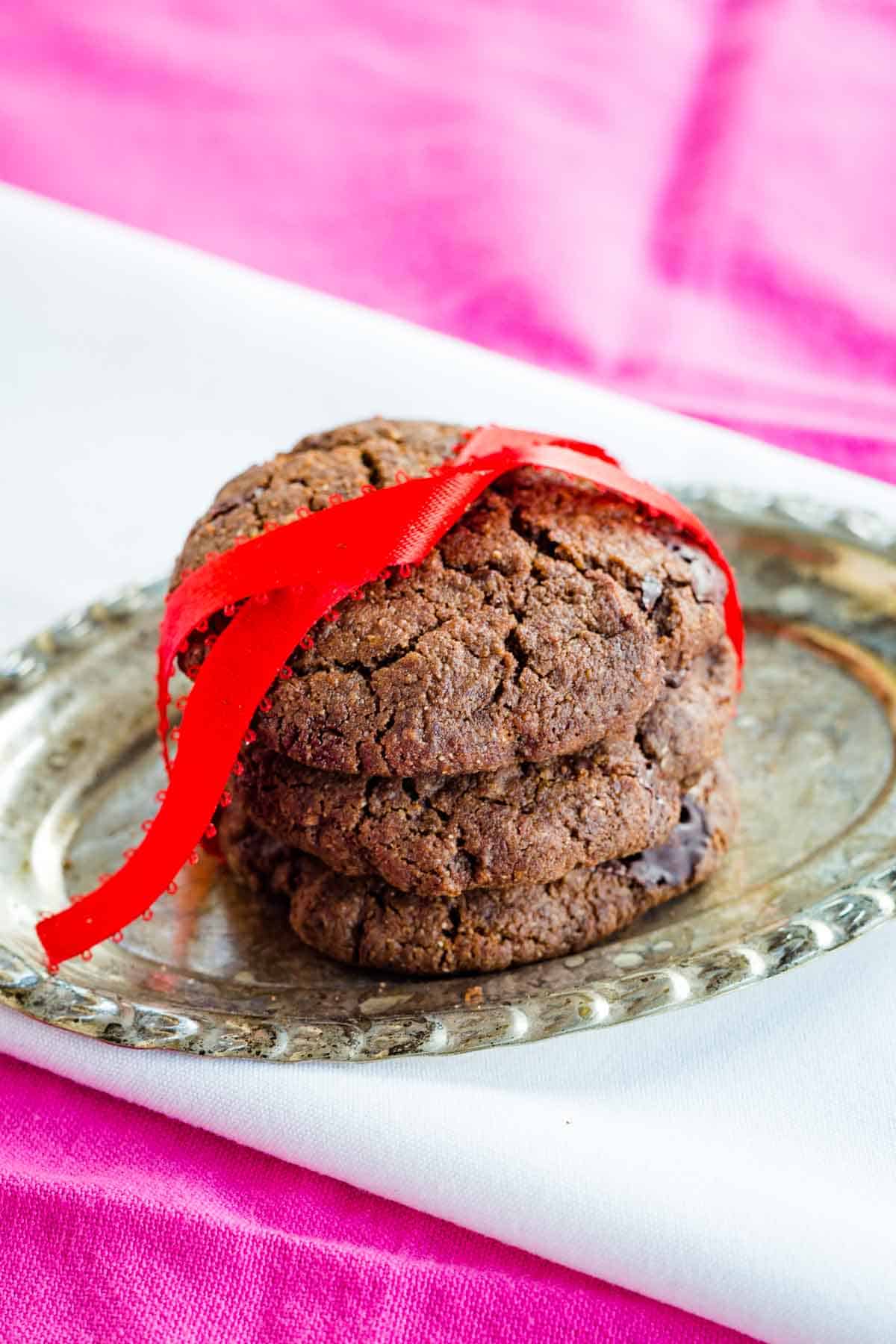 Three chocolate cookies are tied with a red ribbon on a plate.
