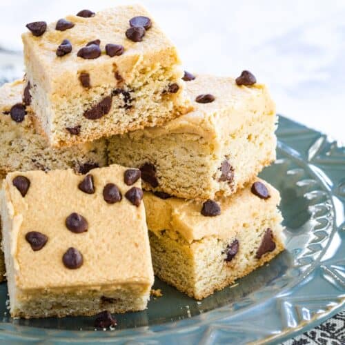 A pile of chocolate chip cookie bars topped with peanut butter frosting and mini chips on a blue plate.