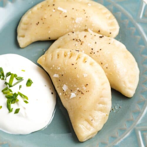 Three pierogi on a plate with a dollop of sour cream garnished with chives.