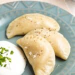 Three pierogi on a plate with a dollop of sour cream garnished with chives with text overlay that says "Gluten Free Pierogi".
