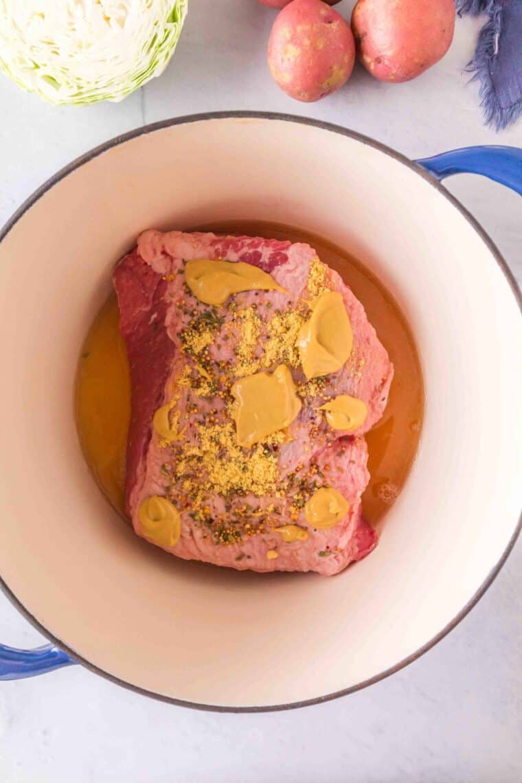 A piece of corned beef is topped with mustard in a dutch oven.