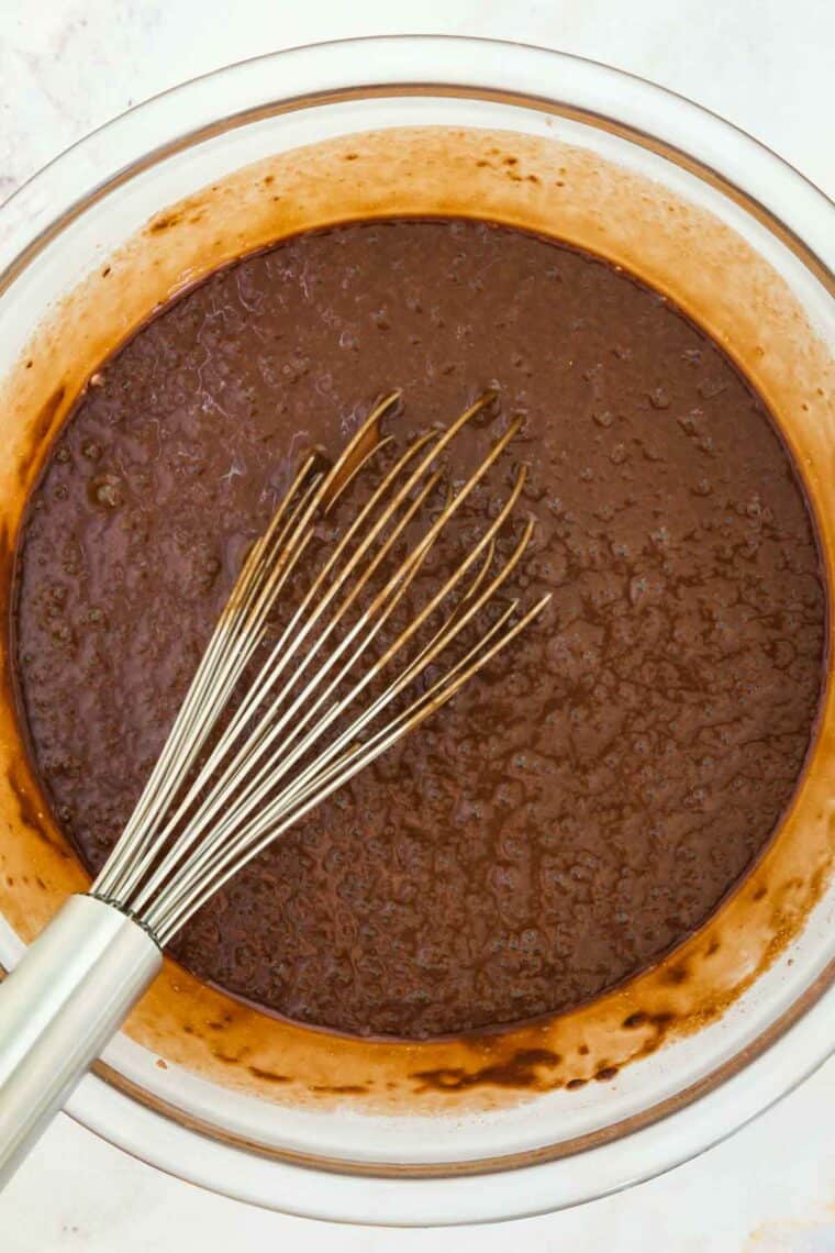 A metal whisk combines chocolate cupcake batter in a glass bowl.
