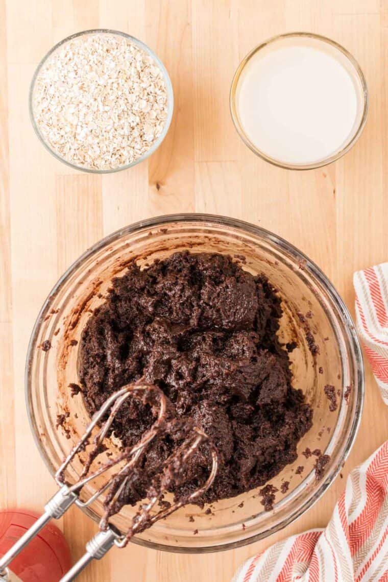 A chocolate batter for brownies is mixed in a glass bowl with a hand mixer.