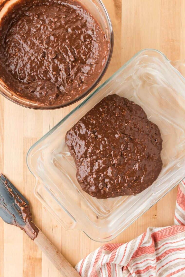 Gluten free protein brownies batter is place in a glass baking dish with the bowl of batter next to it.